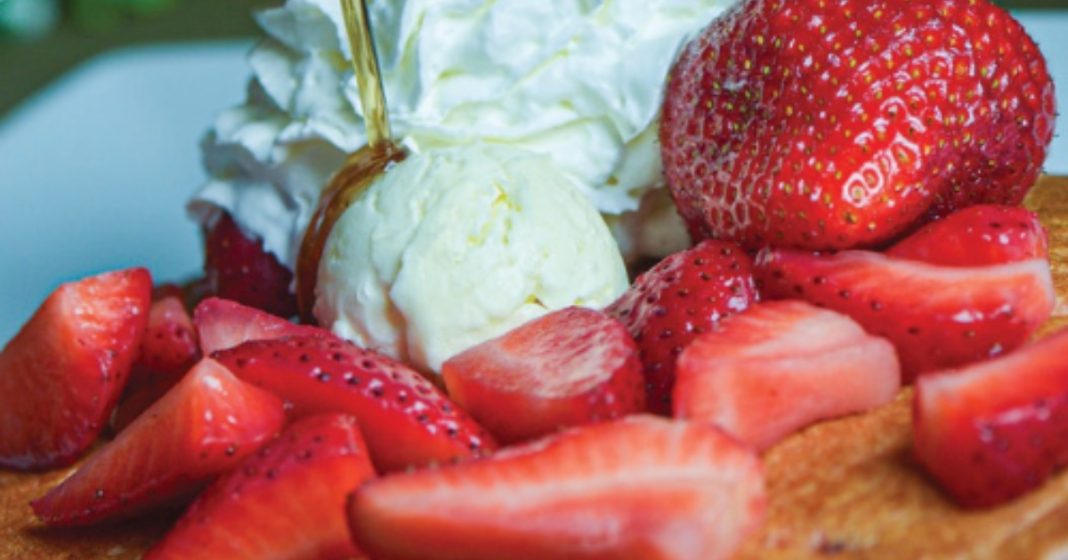 Stack of Johnny Hoe Cakes topped with whipped cream, strawberries, and syrup at Hash House Flamingo Crossings